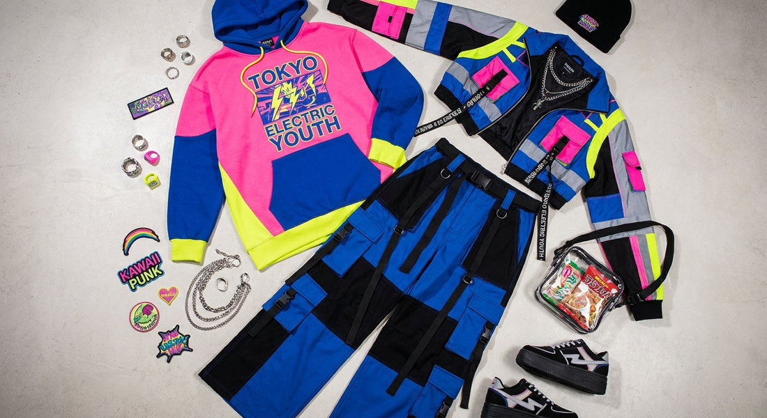 A flat lay editorial arrangement of a Harajuku streetwear outfit including an oversized graphic hoodie, wide-leg cargo pants, and a bold statement jacket surrounded by accessories on a concrete surface.