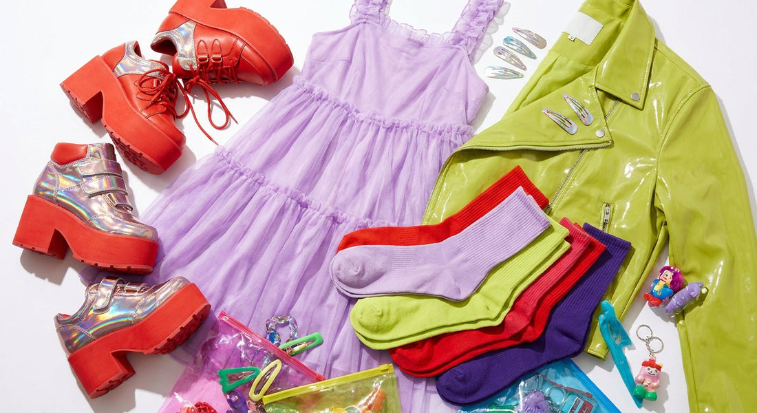 A maximalist flat-lay of colorful Harajuku fashion accessories and clothing in tomato red, chartreuse, lilac, dark purple, and metallic Y2K tones arranged on a white surface.