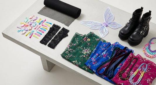 A bird's-eye flat-lay of eclectic Harajuku fashion accessories and clothing pieces representing multiple Japanese street style subcultures, including pastel charms, black lace, platform boots, and sheer floral fabrics.